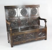 A 17th century carved oak settle, with panel back, open arms and plank seat, W.4ft 3in. Starting