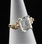 A 14ct gold and aquamarine dress ring, with central emerald cut stone and foliate shoulders, size L.