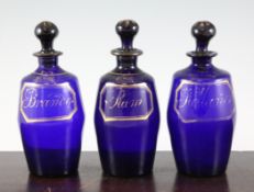 A set of three late Georgian Bristol blue glass and gilt decorated decanters and stoppers, early