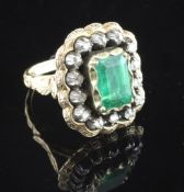 A 19th century gold, emerald and diamond dress ring, the central stone bordered by fourteen