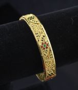 A middle eastern gold filligree and enamel stiff bracelet, with enamelled flowerhead motifs, gross