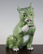 A Masonic faience seated model of an injured cat, with glass inset eyes, green glazed with a white