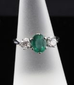 An 18ct white gold, emerald and diamond three stone ring, the oval cut emerald flanked by