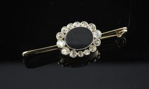 A gold, black onyx and diamond cluster bar brooch, with oval onyx stone bordered by fourteen