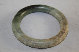A Chinese green jade bangle, carved in relief with an archaistic phoenix and scrolls, the stone with