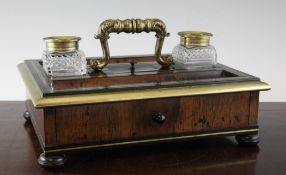 A Regency brass mounted rosewood inkstand, with central scroll cast handle and two cut glass wells