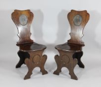A pair of George III mahogany hall chairs, each back painted with an oval panel of a crown and two