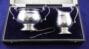 A cased George V silver cream jug and sugar bowl with tongs, of bulbous form, with scroll handles,