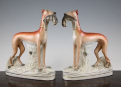 A pair of large Staffordshire pottery figures of greyhounds grasping rabbits, each painted in