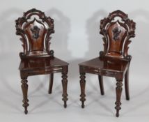 A pair of Victorian carved mahogany hall chairs, with foliate panelled backs on turned legs