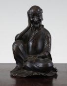 A Chinese bronze seated figure of a Luohan, 18th / 19th century, seated upon his robes and holding a