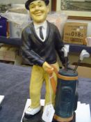 A modern ceramic figurine of Stan Laurel golfing, posed standing with his golf bag that contains