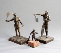 Three bronze figures of tennis players, two of gentleman in striking poses, and a smaller figure