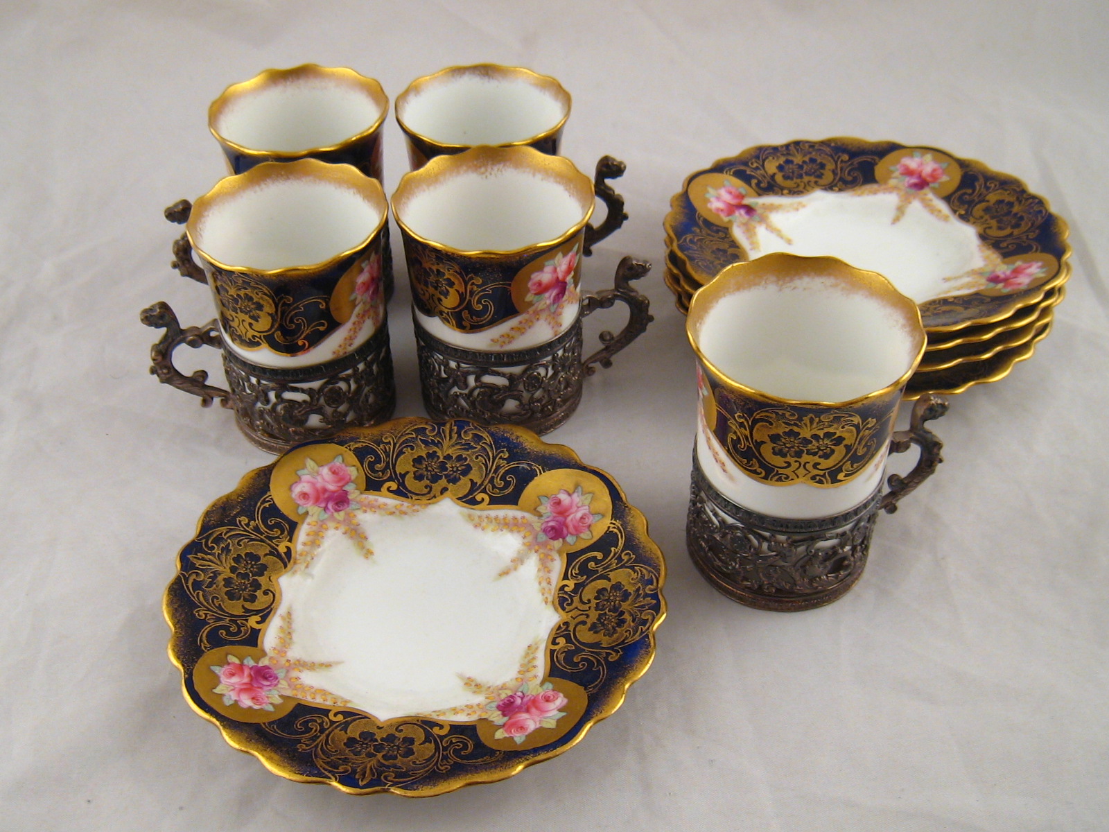 A set of five demi-tasse coffee cups and saucers by Aynsley with silver holders by Charles Bradbury,