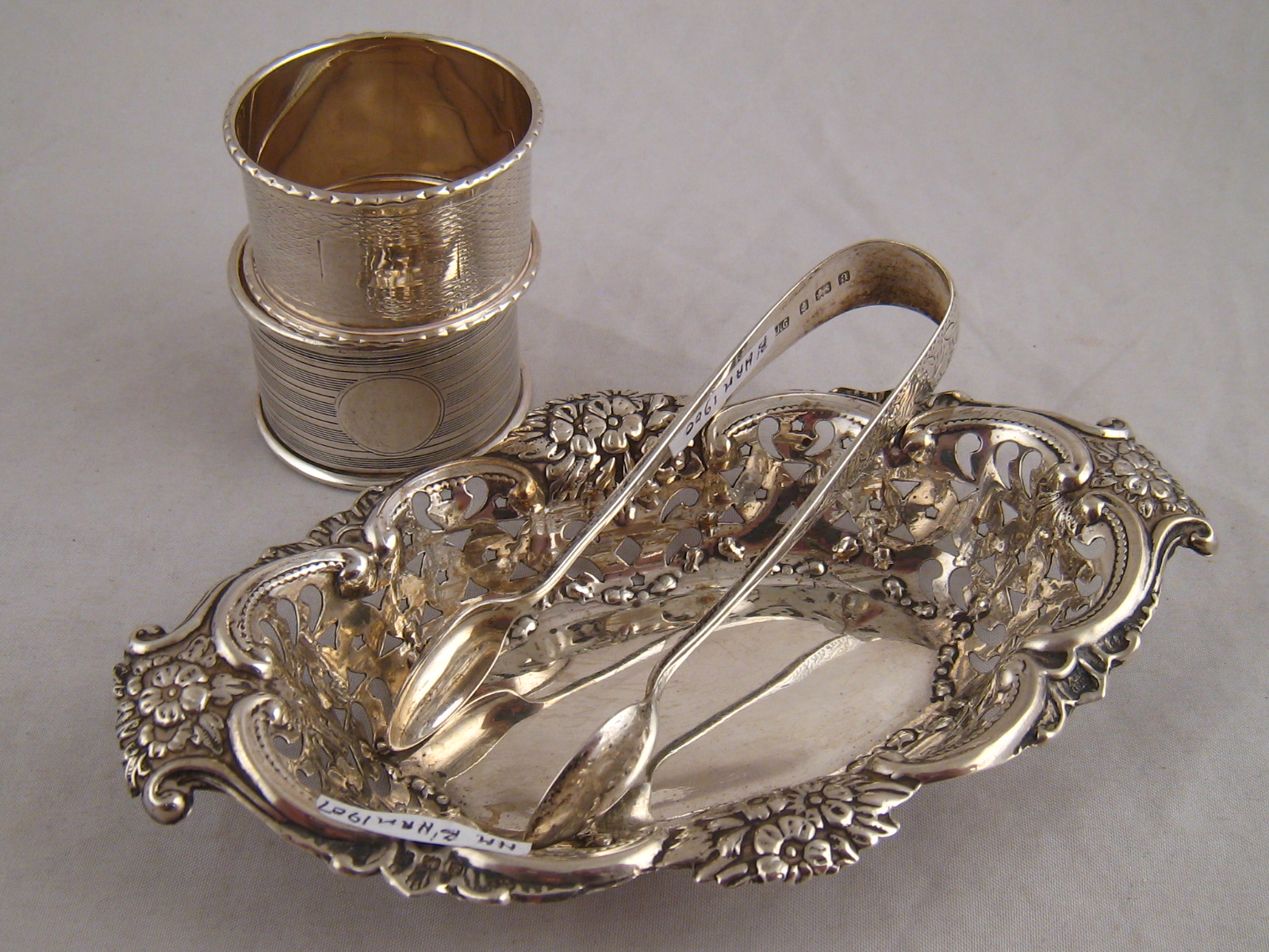 Silver. A pierced bonbon dish, Birmingham 1907,  two napkin rings and a pair of sugar tongs. 99g.