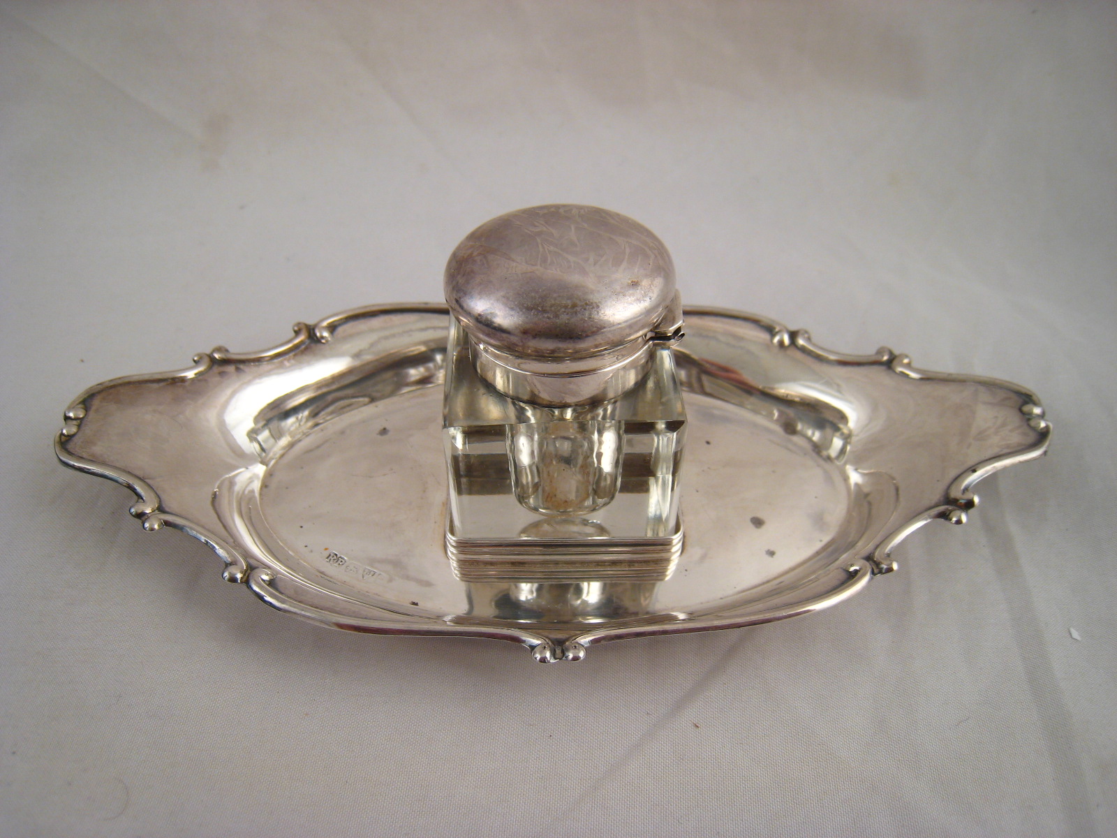 A silver inkstand, the square glass pot with silver mounts on an oval stand with scrolling rim.