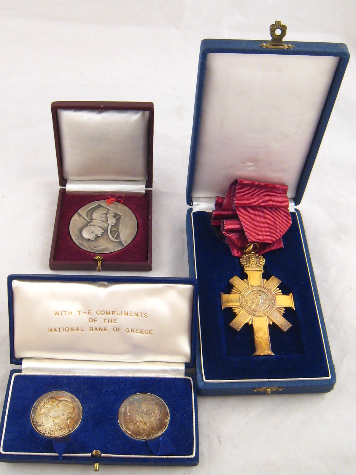 A Greek gilt metal cross with crimson necklace ribbon, two Greek coins dated 1964 in Bank