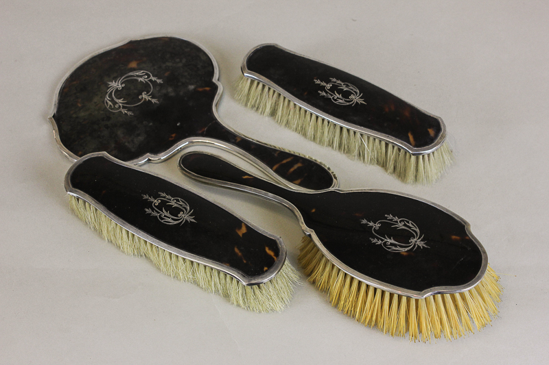 A four piece tortoiseshell and silver back dressing set of hand mirror, hair brush and two clothes