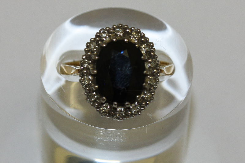 A sapphire and diamond cluster ring, the oval cut stone claw set within a border of single cut