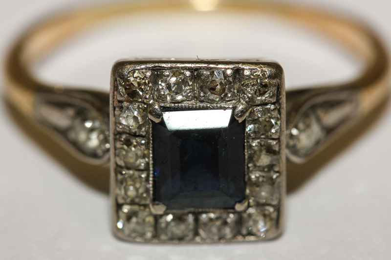 A sapphire and diamond ring, the square sapphire with diamond border on 18ct gold shank