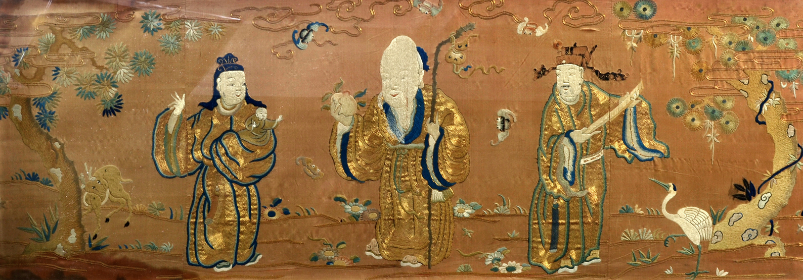 A probably 18th century Chinese embroidered silk panel, depicting three immortals, in gold, indigo