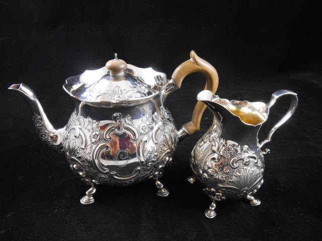 A late Victorian embossed silver teapot, shaped wooden handle, four paw feet, together with the