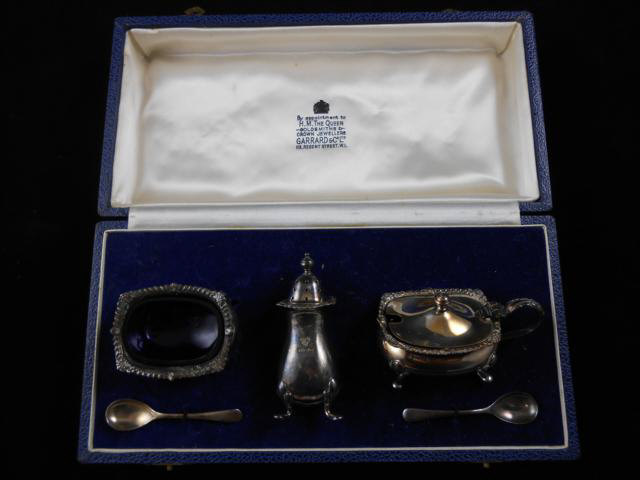 A Garrard & Co silver condiment set comprising pepper, salt and mustard with two silver spoons -