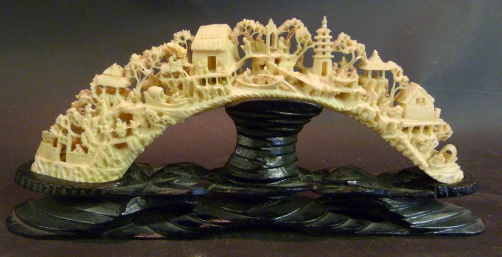 A Chinese Carved Ivory Tusk, decorated in relief with a landscape scene upon a hardwood shaped