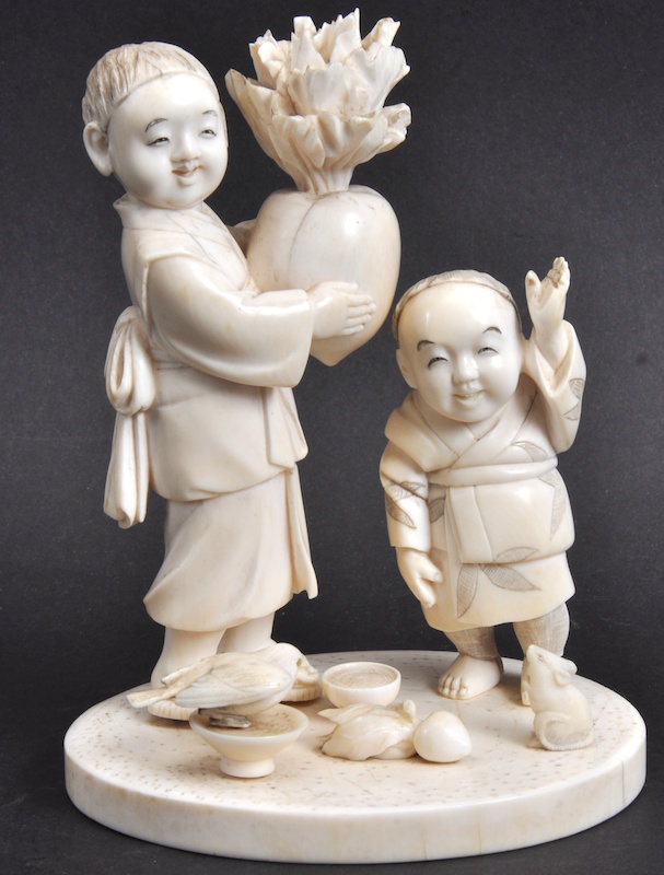 AN EARLY 20TH CENTURY JAPANESE MEIJI PERIOD IVORY OKIMONO depicting two figures holding fruit.