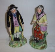Pr Staffordshire figurines of gentleman on crutches wearing a black flock coat & lady carrying