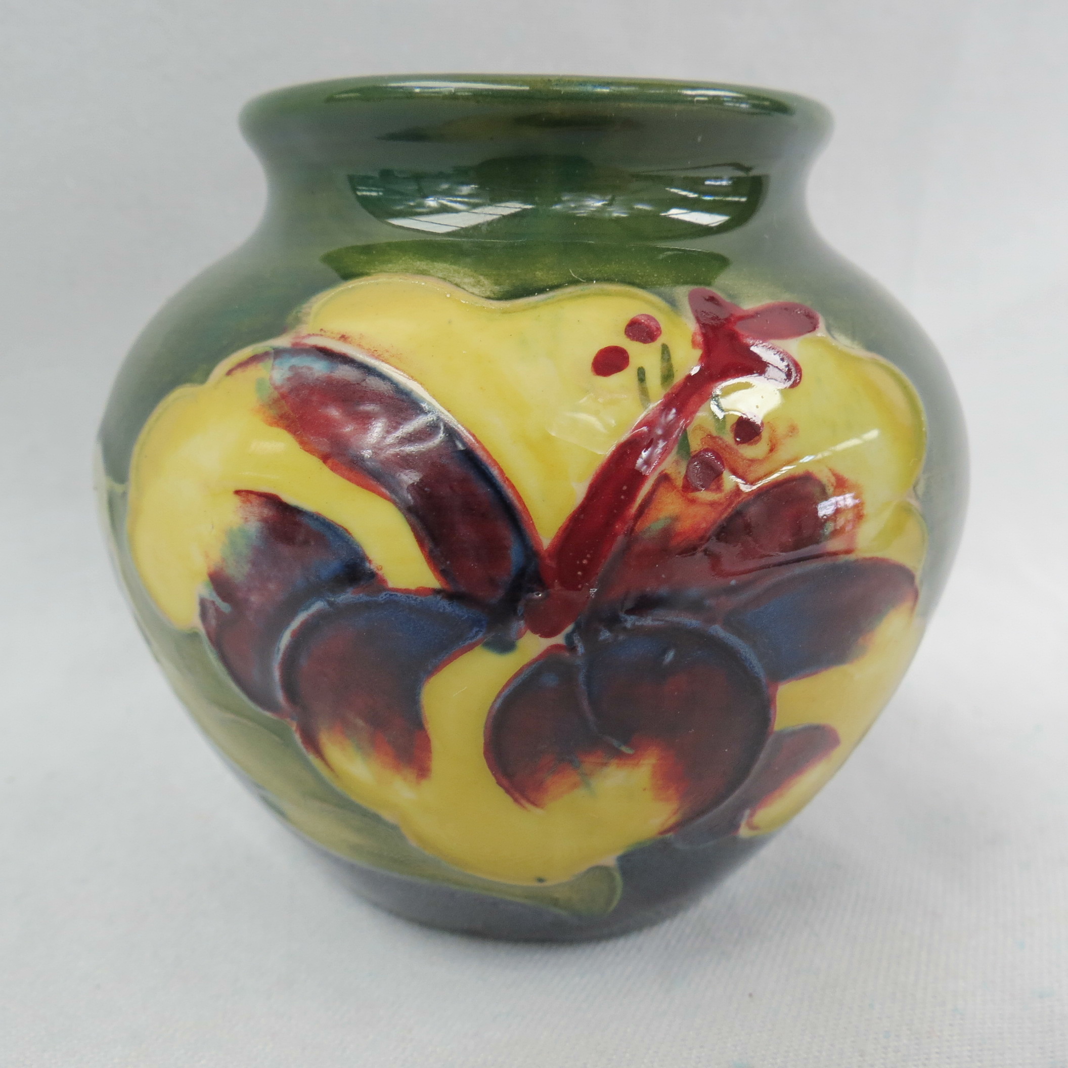 A small Moorcroft vase, hibiscus pattern on a green/blue ground, bearing remains of a paper label to