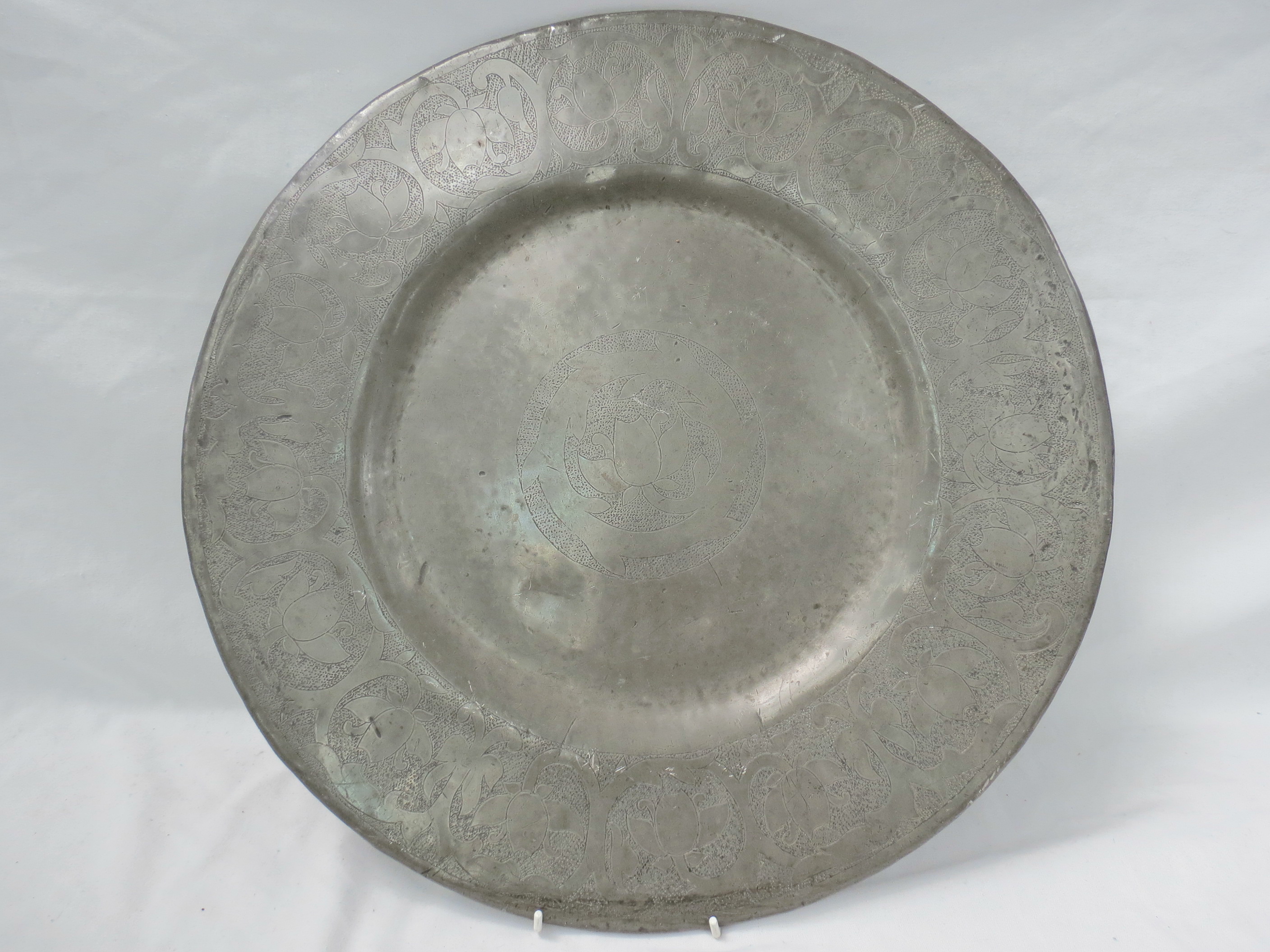 A late 19thC pewter charger with a central floral and foliate motif, within a broad border of a