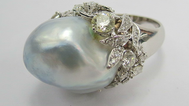 A large Baroque pearl of a grey hue in white metal setting. Wreath of assorted size diamonds, claw