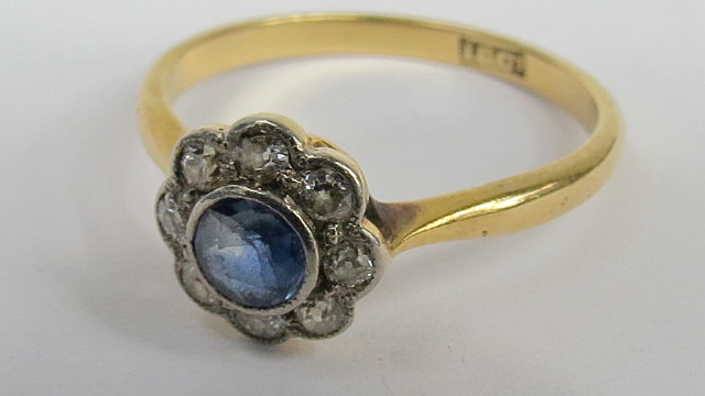 A sapphire and diamond daisy cluster central sapphire in rub over setting with gallery of millegrain