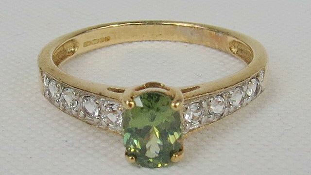 A 9ct gold ring, oval green stone with gallery of white stones set in each shoulder.