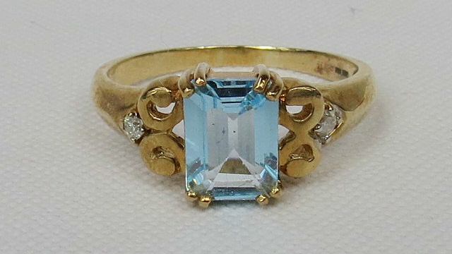 A 9ct gold trap cut topaz (untested) dress ring with small diamond set in each scrolled shoulder.