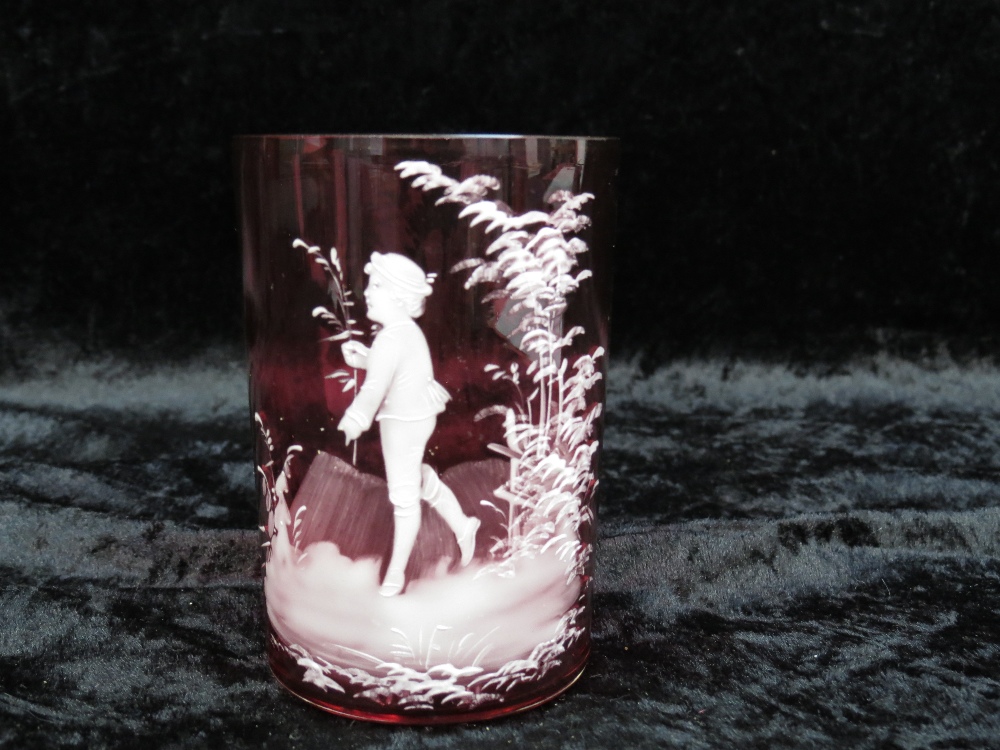 A cranberry glass beaker with Mary Gregory decoration of a boy in foliage.