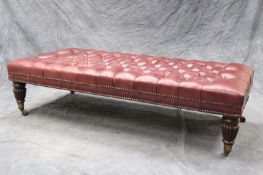 A large leather upholstered stool, in oxblood leather with deep button upholstery, on short reeded