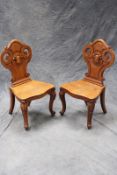 A pair of Victorian carved oak hall chairs, each with pierced shaped back with central shield