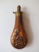 An embossed copper powder flask, decorated with birds and trees to either side, graduated nozzle