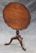 A carved mahogany tilt-top table, the pie crust circular top on baluster turned column, trefid