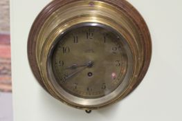 An eight day ship’s clock, with 6 inch dial, in brass case and bezel, on wooden plaque, marked