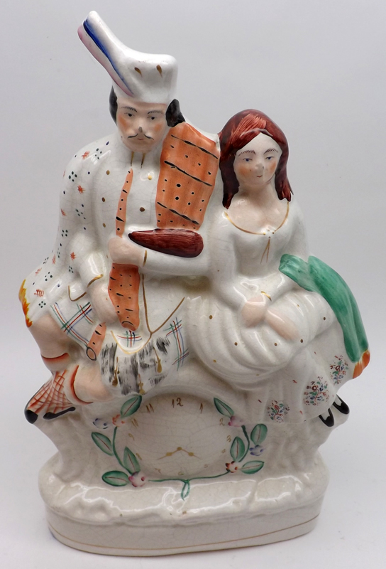 A 19th Century Staffordshire Figure Group, modelled as a Scots couple seated on a painted clock