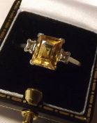 A precious metal Ring set with a centre Square Cut Topaz, flanked to each side by a small Baguette