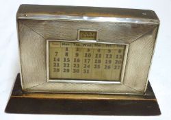 A George V Perpetual Desk Calendar of typical rectangular form, raised on an ebonised wooden base,