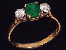 An 18ct Gold and Platinum central Emerald Cut Emerald and two Brilliant Cut Diamond Ring, the centre