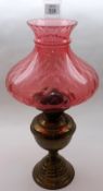 An early 20th Century Oil Lamp with Cranberry Glass Shade, clear glass chimney and a brass body on a