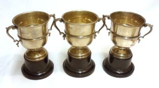 A group of three early 20th Century Trophy Cups of typical double-handled form, raised on ebonised
