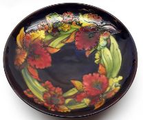 A large Moorcroft Round Shallow Pedestal Bowl, decorated with an orchid pattern on a blue