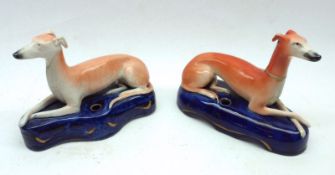 A pair of Staffordshire Inkwells, modelled as recumbent greyhounds decorated in orange and blues; 7”